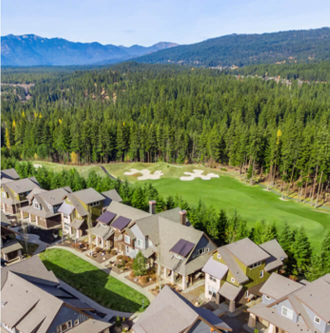 Aerial view of a row of houses bordering a stunning golf course at Suncadia, surrounded by dense forest, with mountains visible in the distance under a clear sky. Nearby, Cle Elum's restaurants offer delightful culinary experiences to complement this serene Washington escape.