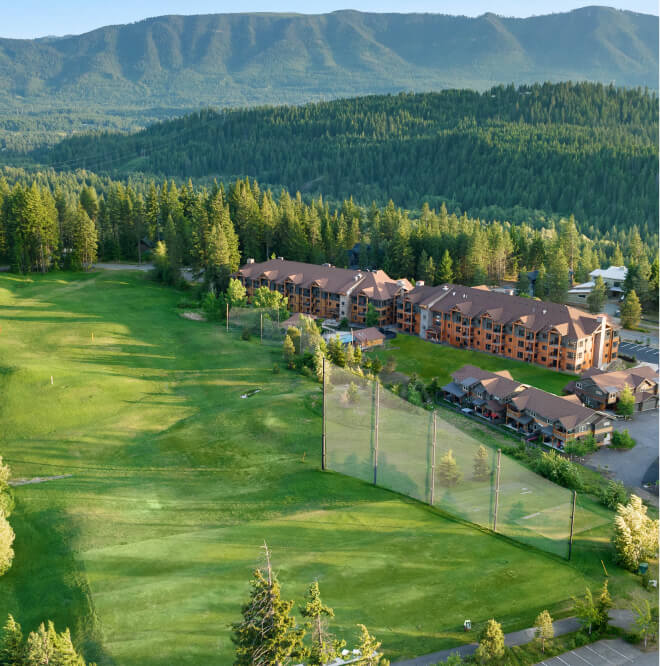 An aerial view of Suncadia Resort in Washington showcases a stunning golf course with a hotel and majestic mountains in the background, all embraced by dense forest. Nearby, visitors can explore Cle Elum restaurants to savor local flavors amidst this serene landscape.