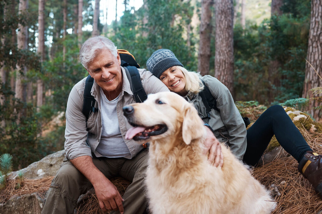 An older couple sits in the forest with a happy golden retriever, enjoying the tranquility near Suncadia Resort Washington. They are wearing backpacks and casual outdoor clothing, perfectly suited for their outdoor adventure.