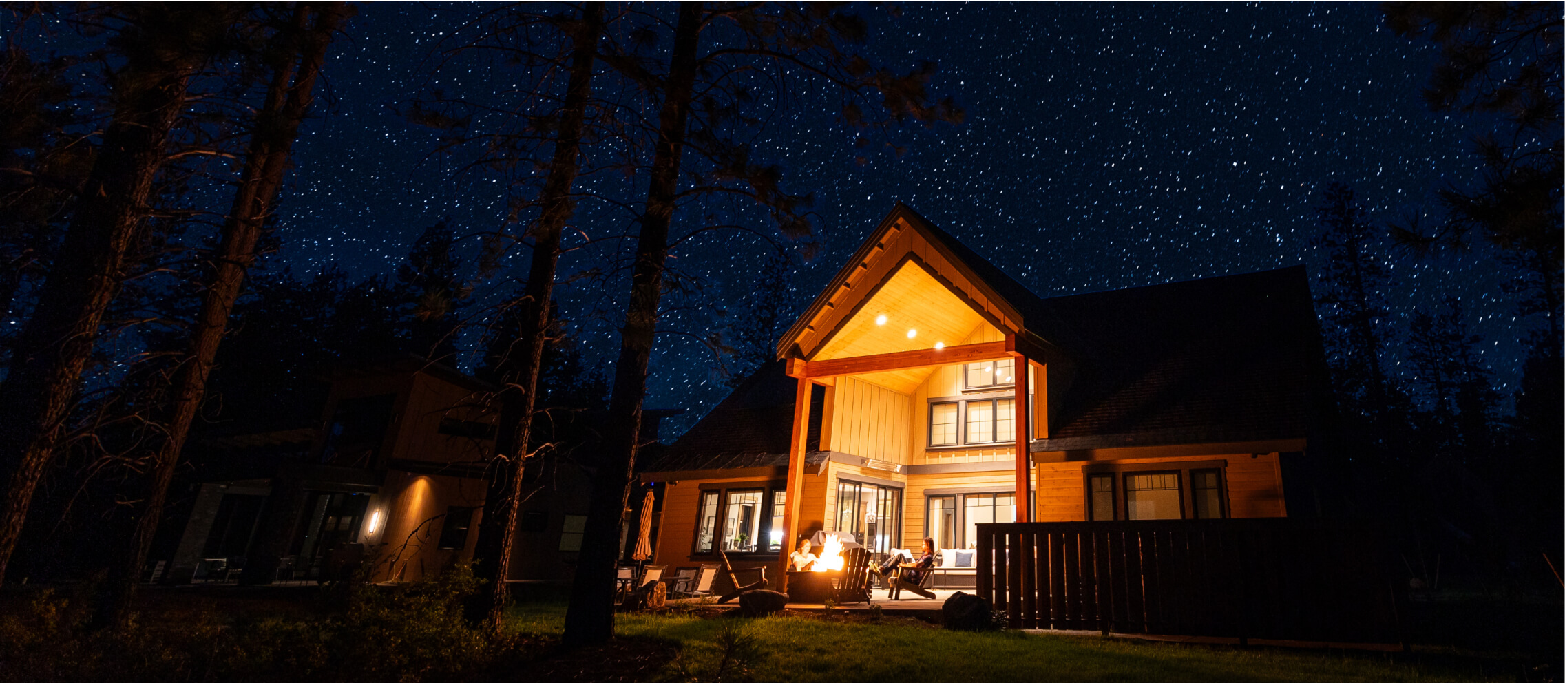 A wooden cabin with an illuminated porch stands under a starry night sky, surrounded by tall trees, epitomizing the secluded charm of Suncadia Resort.