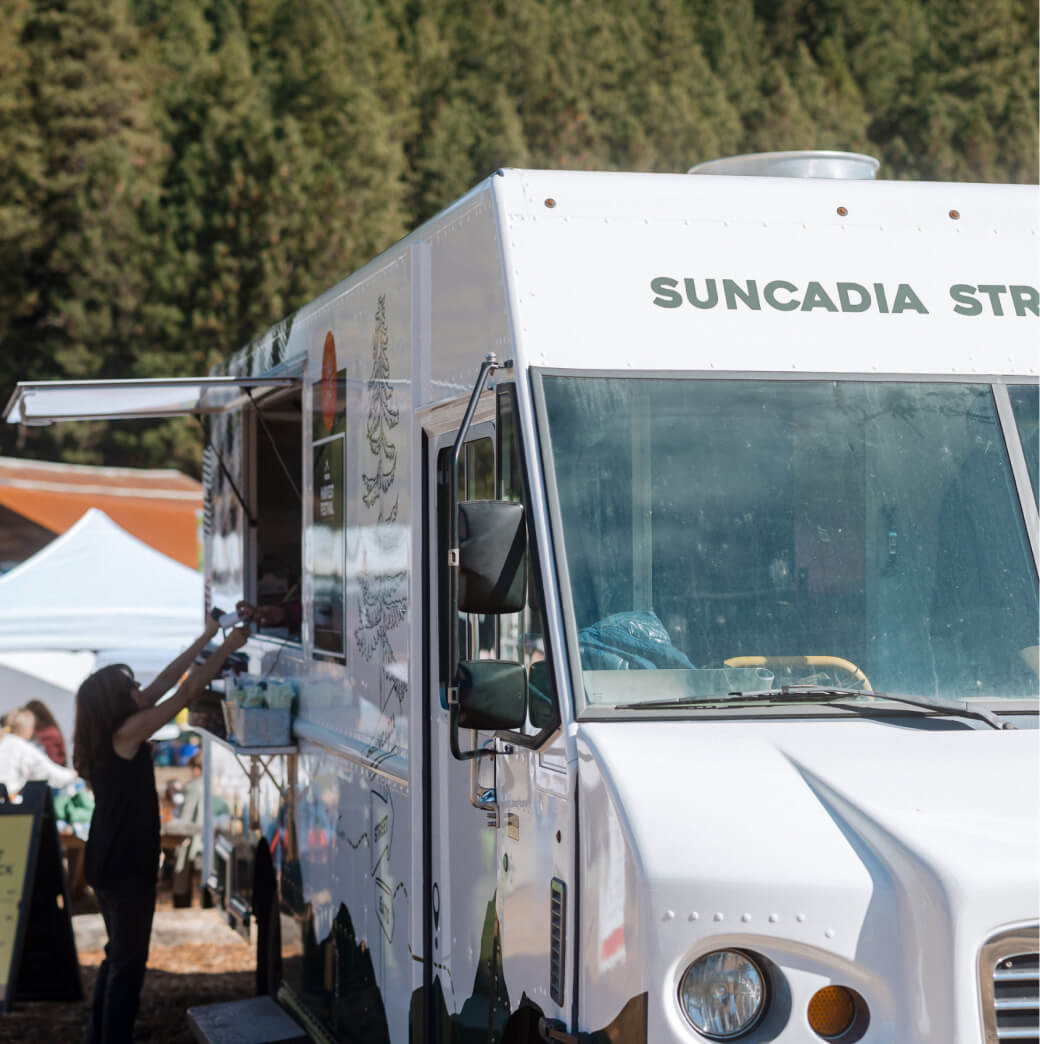 A person orders from a white food truck parked outdoors, surrounded by trees—a charming scene reminiscent of the relaxed vibe you'll find near Suncadia homes and Cle Elum restaurants.