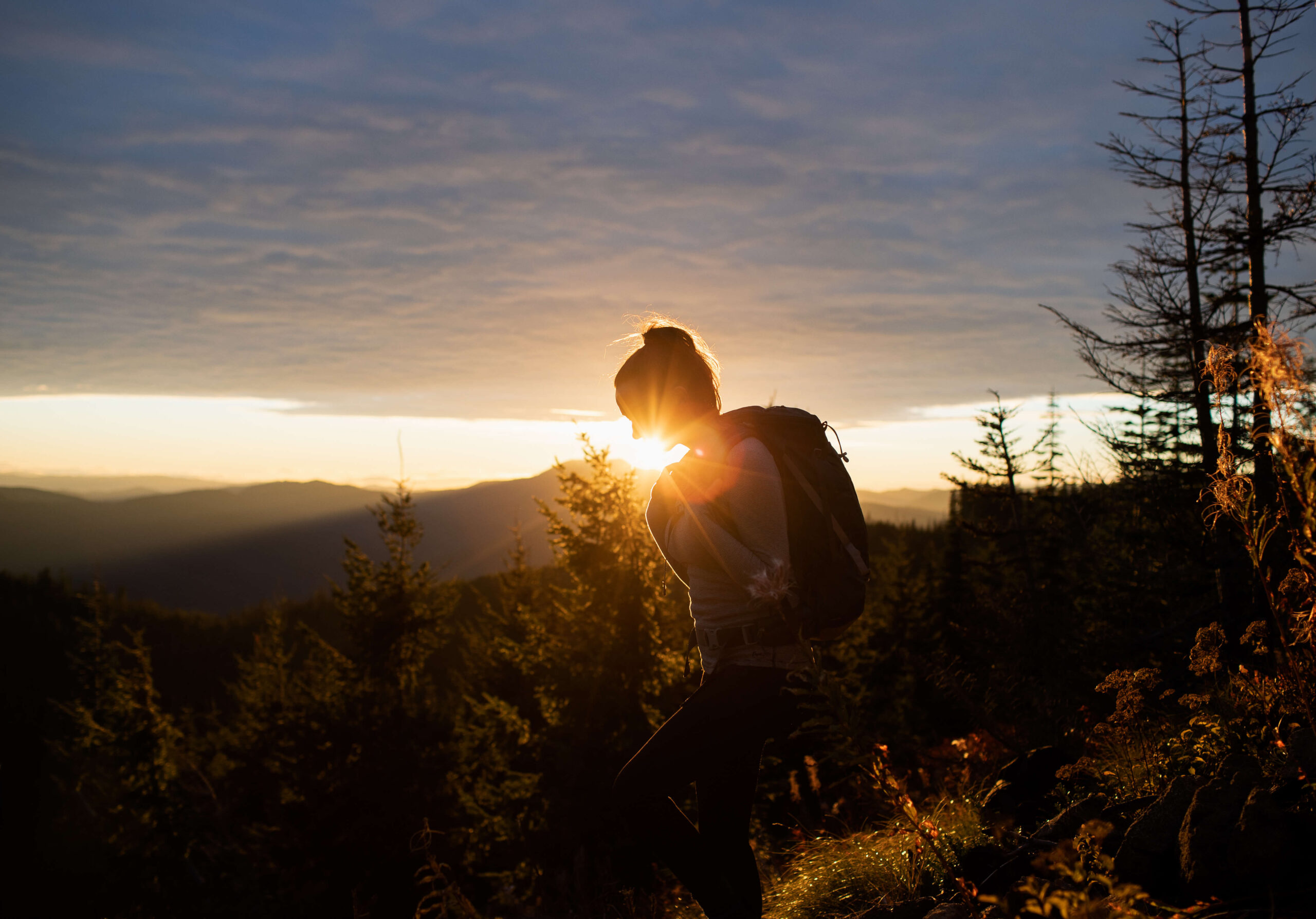 A silhouette of a person with a backpack meanders along a trail, silhouetted against the breathtaking sunset over Suncadia Resort's mountainous scenery, where nature and serenity intertwine seamlessly.