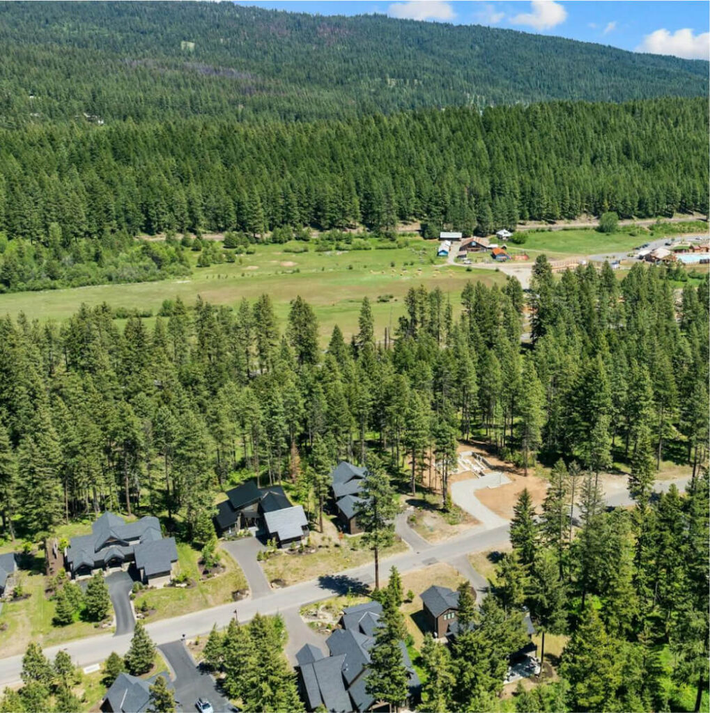 Aerial view of a forested area with residential houses and a road, surrounded by lush greenery and rolling hills under a blue sky with clouds. Nearby, enjoy the charm of Cle Elum restaurants or explore Suncadia real estate opportunities.