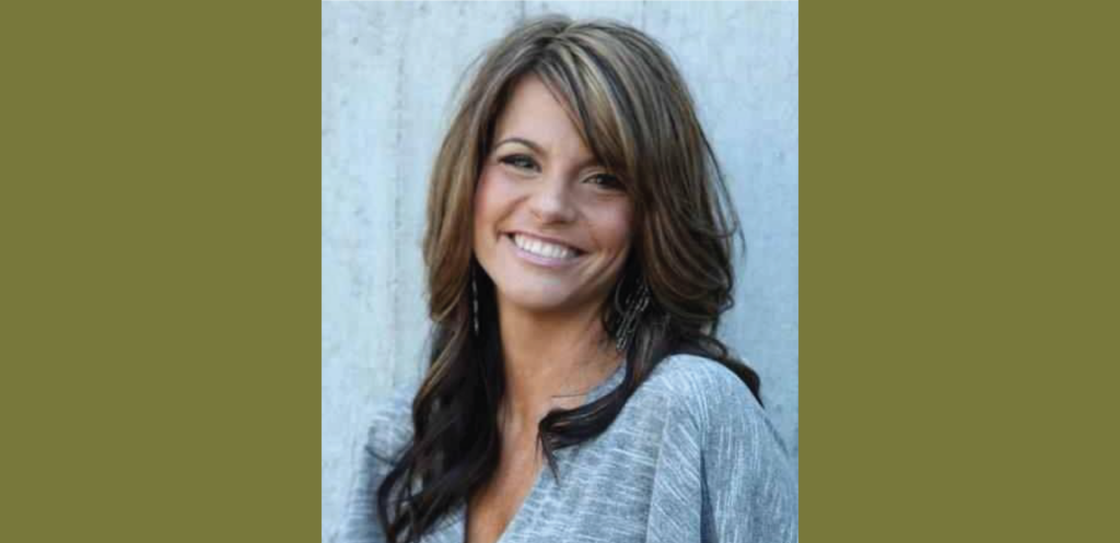 A woman with long brown hair and highlights, wearing a gray top, smiles warmly in front of a plain background, radiating the inviting charm of Suncadia Resort.