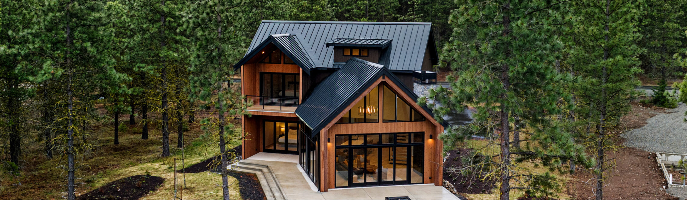 A modern two-story house with large windows and a black metal roof, nestled among dense pine trees in the serene Suncadia area, offers easy access to nearby Cle Elum restaurants.