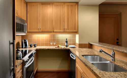 Modern kitchen with wooden cabinets, stainless steel appliances, and a granite countertop, reminiscent of the elegant designs found in Suncadia Resort Washington. Wine bottle, glasses, and cutting board on the counter complement the beige tiled backsplash.