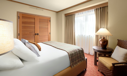 A hotel room with a neatly made bed, wooden headboard, and side table with a lamp invites relaxation. Closed wooden closet doors and a curtained window evoke warmth, akin to the charming interiors of Suncadia homes nestled near Cle Elum restaurants.