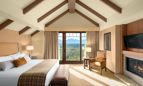 A cozy hotel room at Suncadia Resort with a vaulted ceiling, featuring a large bed, a fireplace, a TV, and a window with breathtaking mountain views.