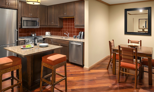 A modern kitchen with stainless steel appliances and a granite island featuring two barstools serves as the heart of this Suncadia real estate gem. Wooden cupboards complement the adjacent dining area with a table, four chairs, and a stylish wall mirror.