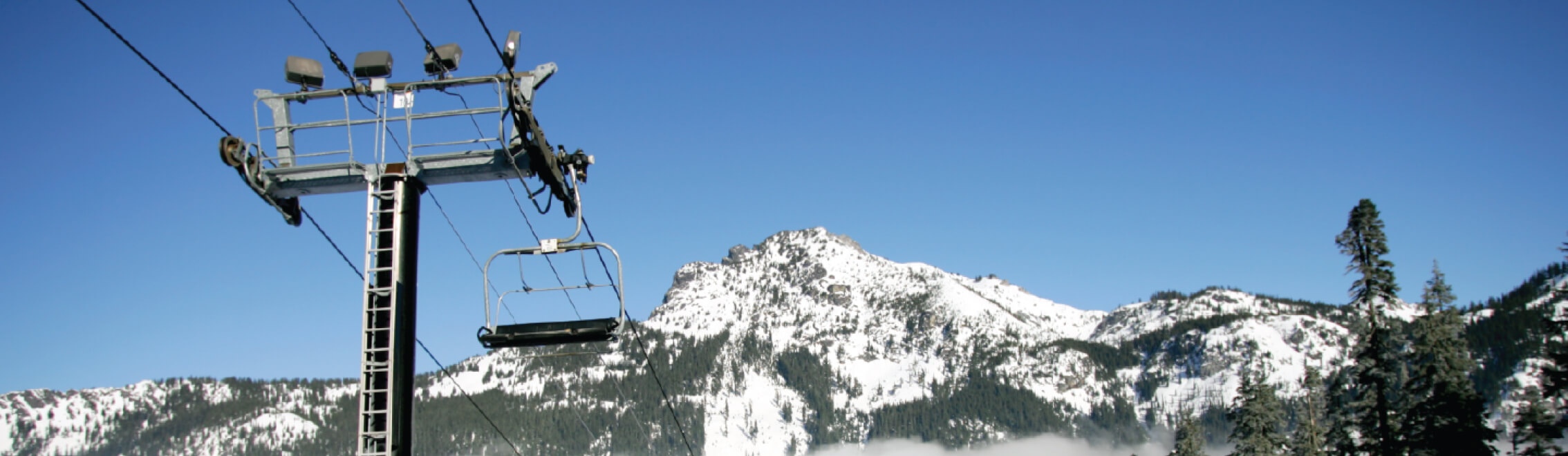 A ski lift glides up the snowy mountain under a clear blue sky, offering breathtaking views of Suncadia Resort in Washington, where cozy Suncadia homes nestle amidst winter wonderlands.