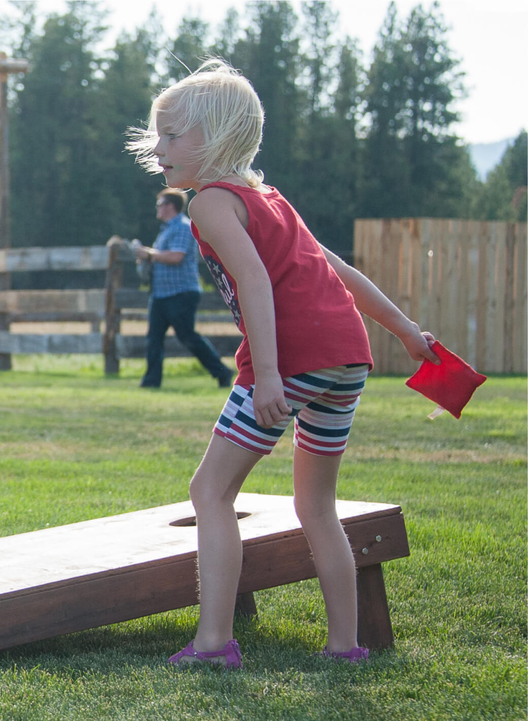 A child in a red tank top plays cornhole on the lush, green lawn at Suncadia Resort, while another person strolls through the picturesque background.