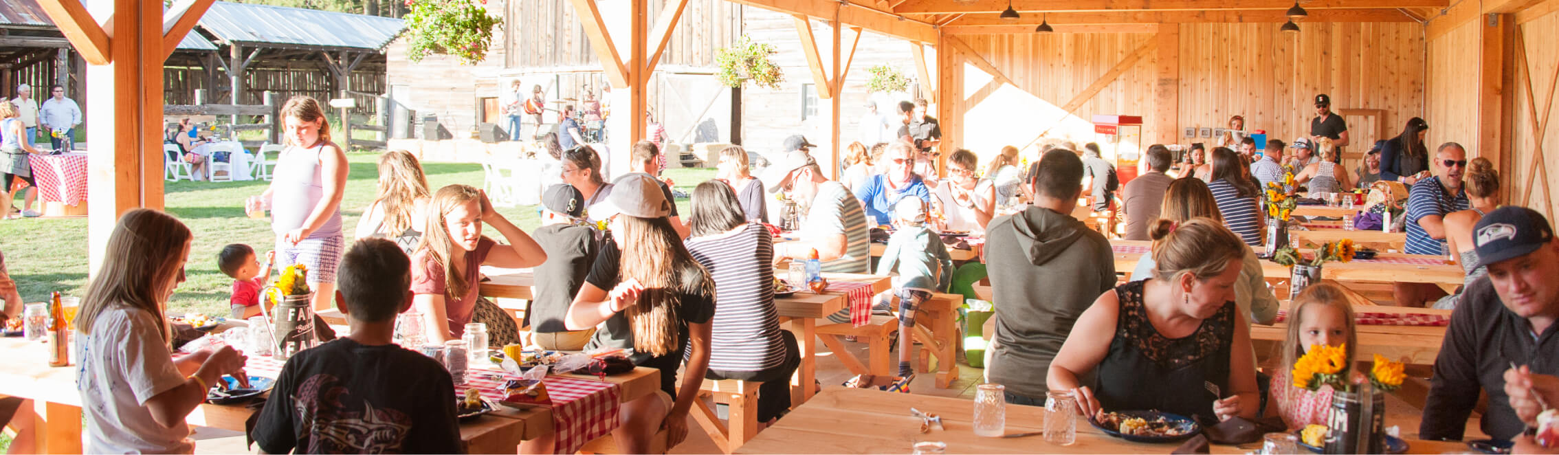 A group of people attending a gathering at a picnic area with wooden tables, under an open structure at Suncadia Resort, surrounded by a lush grassy landscape.