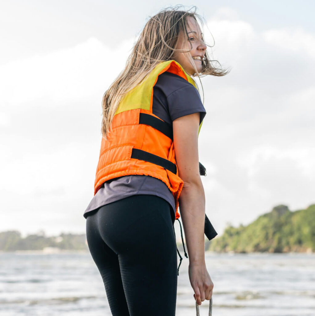 A person wearing an orange life jacket stands near the water at Suncadia Resort, Washington, holding a rope against a backdrop of sky and trees.