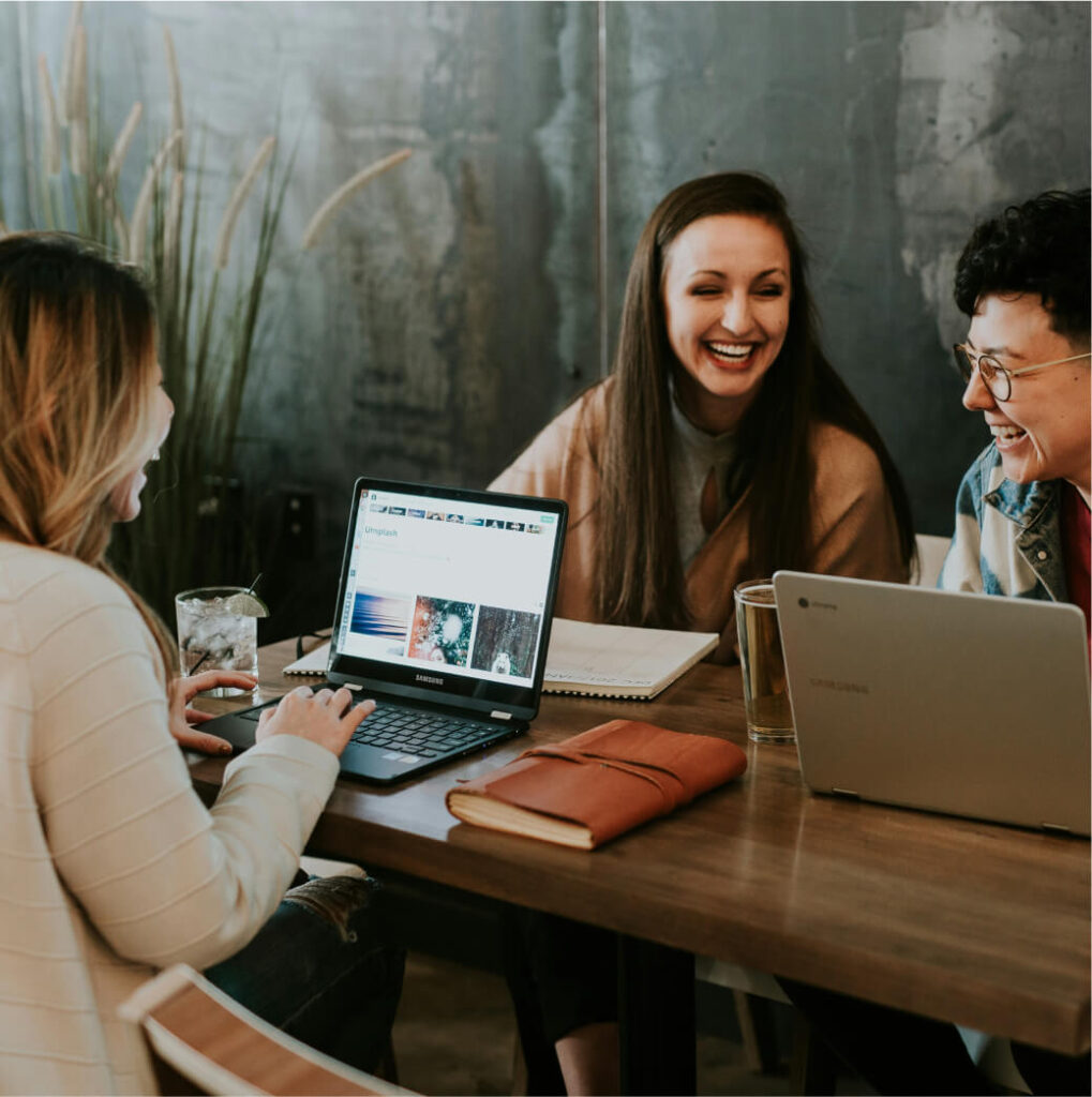 Three people sitting at a table with laptops, notebooks, and drinks, engaging in a lively conversation about the best Cle Elum restaurants to visit during their stay at Suncadia Resort.