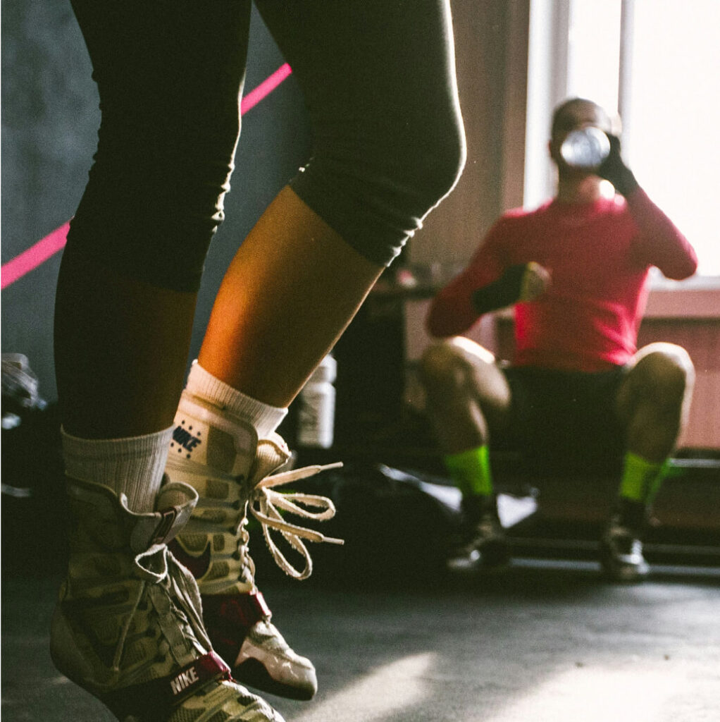 Close-up of a person wearing boxing shoes and jumping rope in a gym, reminiscent of the energetic vibe found in Cle Elum restaurants, with another person in the background sitting and drinking from a bottle.