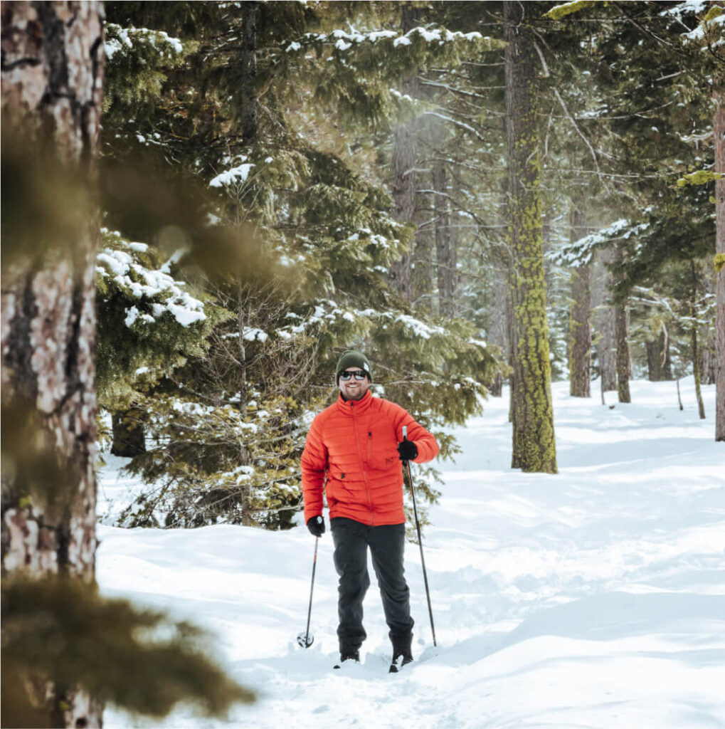 A person in an orange jacket is snowshoeing through a snowy, forested area near the picturesque Suncadia Resort in Washington.