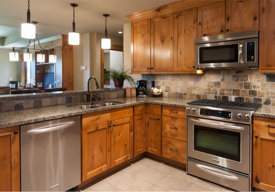 Rustic kitchen in a charming Suncadia home, featuring wooden cabinets, granite countertops, stainless steel appliances, and pendant lighting. The tiled backsplash complements the warm-toned cabinetry, offering an inviting atmosphere typical of Suncadia real estate.