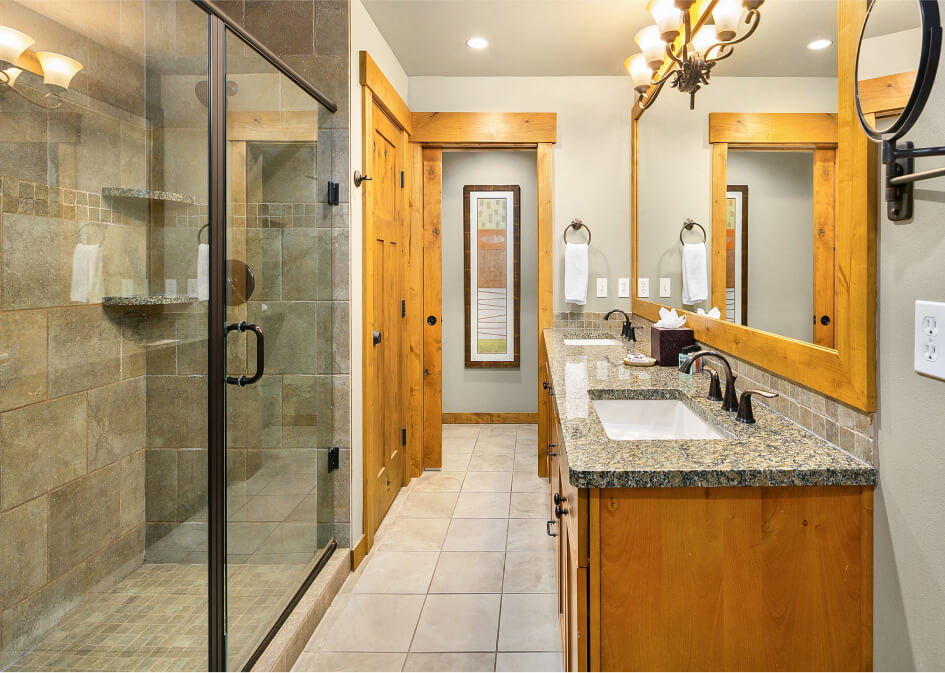 Suncadia Resort bathroom featuring a large glass-enclosed shower, dual sinks with a granite countertop, wooden cabinets, and decorative lighting fixtures.