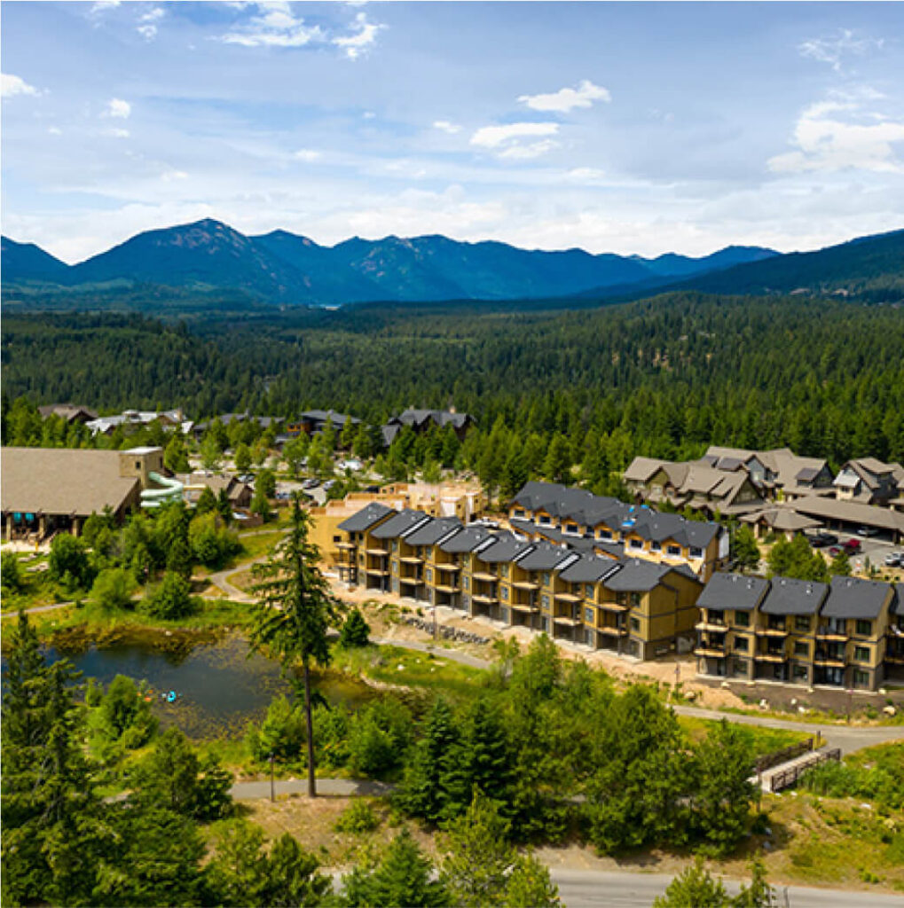 Aerial view of Suncadia Resort Washington, showcasing a mountain retreat with several buildings nestled among lush trees, a small pond reflecting the azure sky, and distant mountains. Nearby, Cle Elum restaurants offer delightful dining experiences in this serene setting.