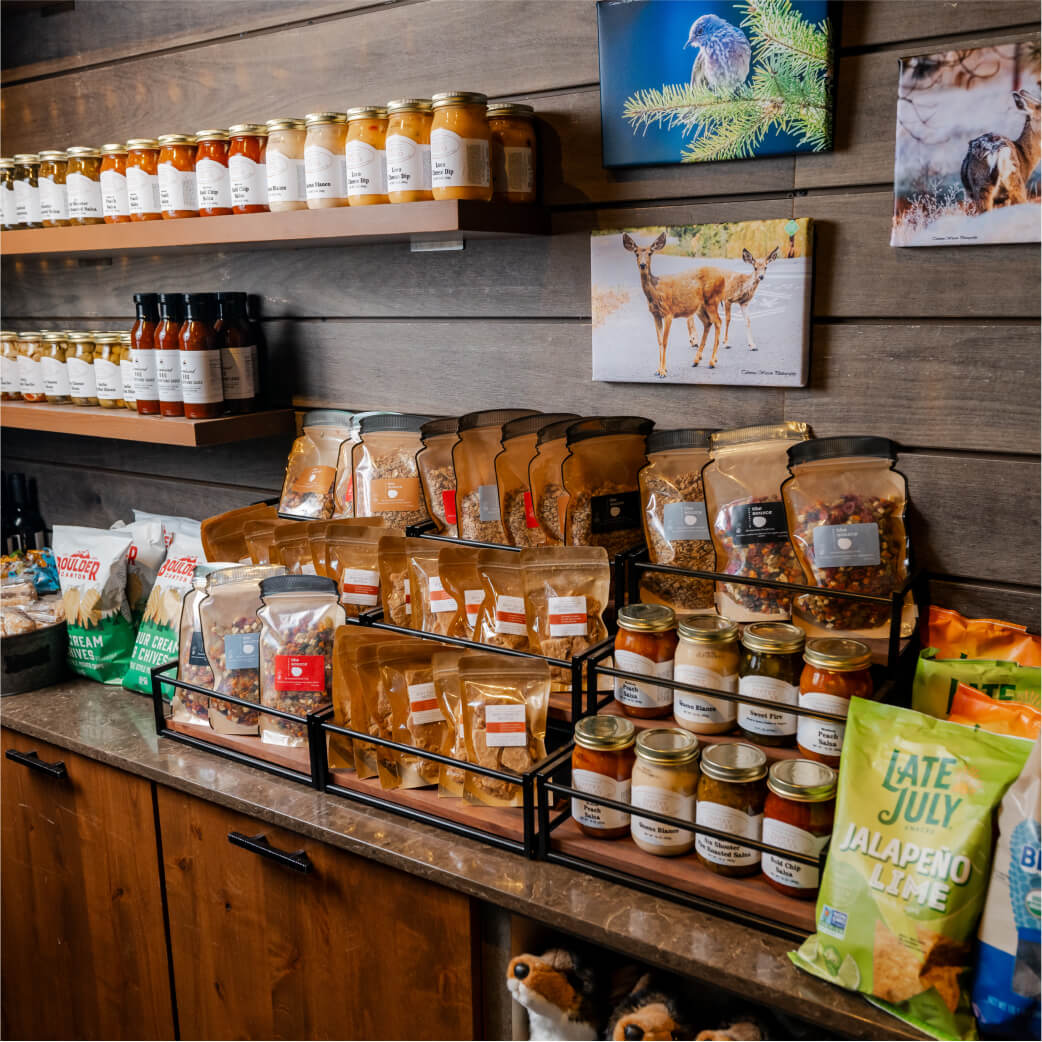 A rustic shop display at Suncadia Resort, Washington, features shelves brimming with jars of honey, sauces, packaged snacks, and spices. The wall behind showcases captivating wildlife photos, echoing the natural beauty surrounding the renowned Cle Elum restaurants nearby.