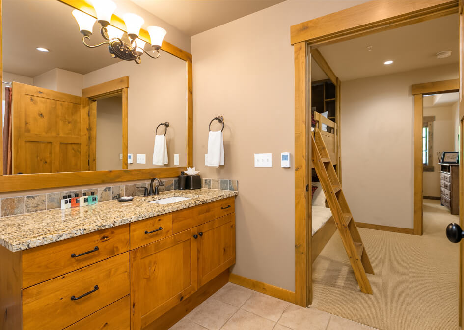 This Suncadia real estate gem features a bathroom with wooden cabinets, a granite countertop, and dual sinks. A ladder leads to a loft in the adjacent room, offering a unique touch to this beautiful home.