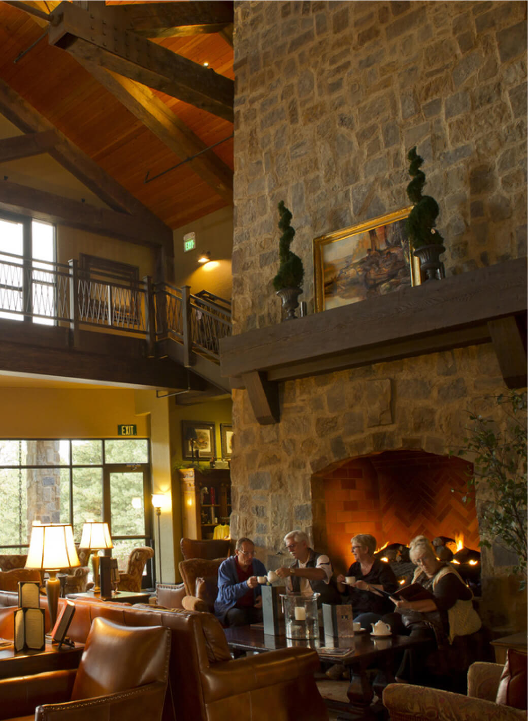 At Suncadia Resort, a cozy sitting area welcomes you with people gathered around a table in front of a large stone fireplace. Surrounded by leather seats and warm lighting, it exemplifies the inviting charm of Suncadia homes.