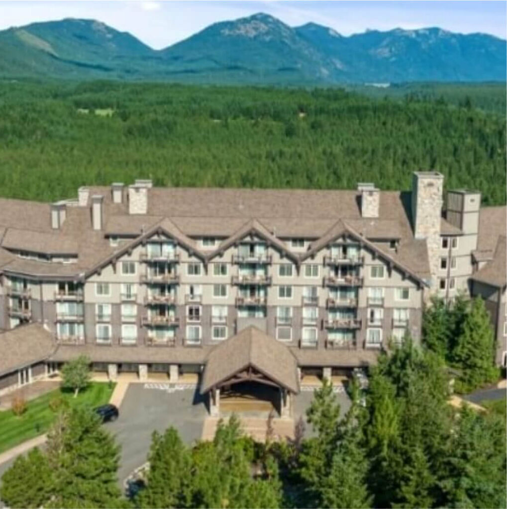 A large lodge set in a forested area with mountains in the background, just a stone's throw from Suncadia Resort Washington, offers easy access to Cle Elum restaurants brimming with local flavors.