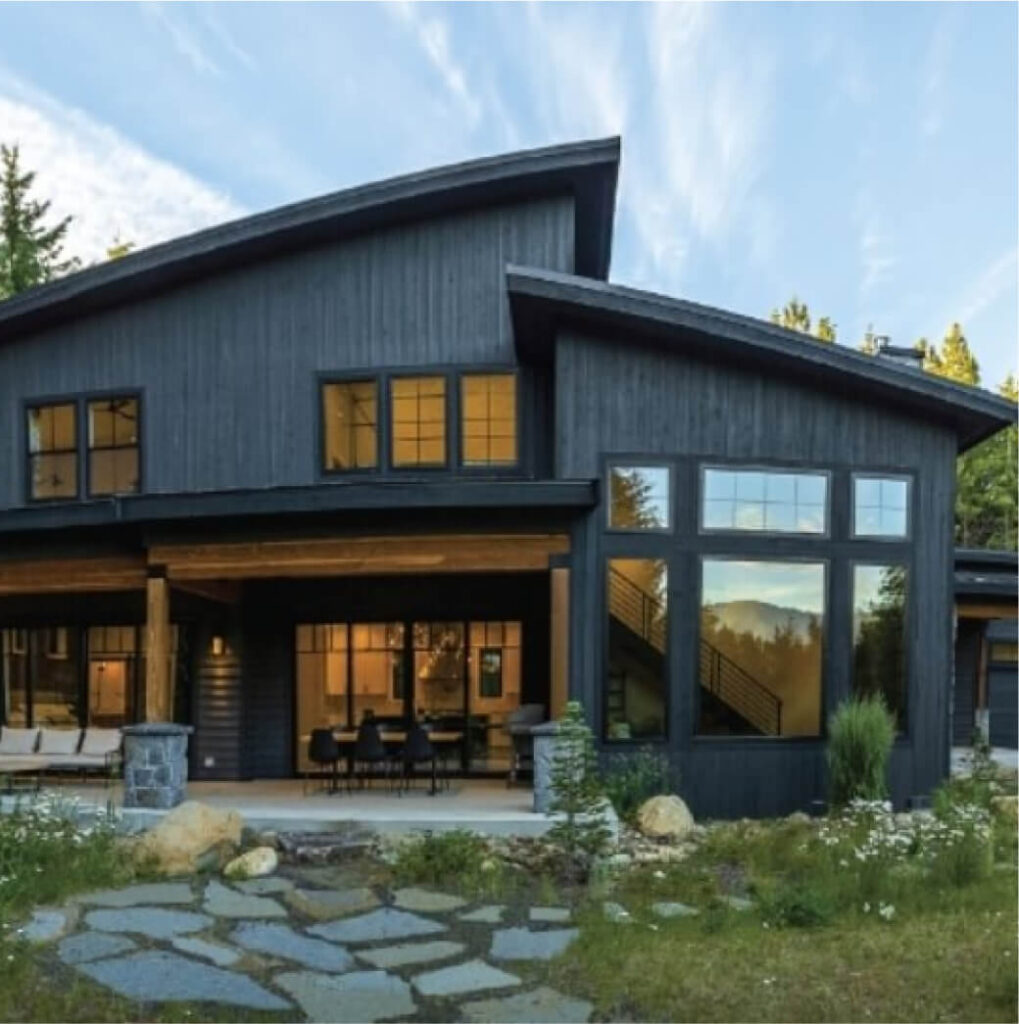 Modern house with dark wood exterior, large windows, and a stone path leading to the entrance, nestled among greenery and trees in the serene Suncadia real estate region.