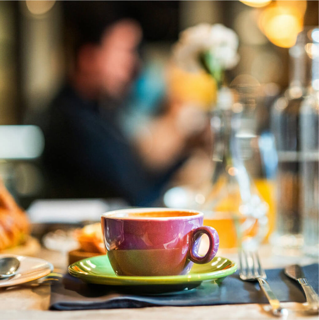 A cup of coffee sits on a green saucer on a table at one of the cozy Cle Elum restaurants, surrounded by a knife, a fork, and a blurred background.