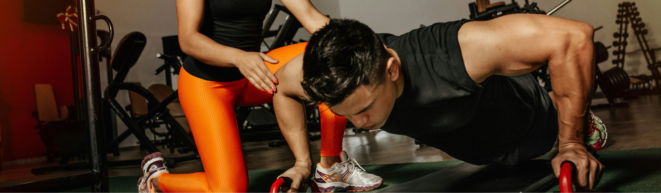 A person in a black tank top does push-ups on bars while another in orange leggings supports them from the side, embodying the dynamic energy found at Suncadia.