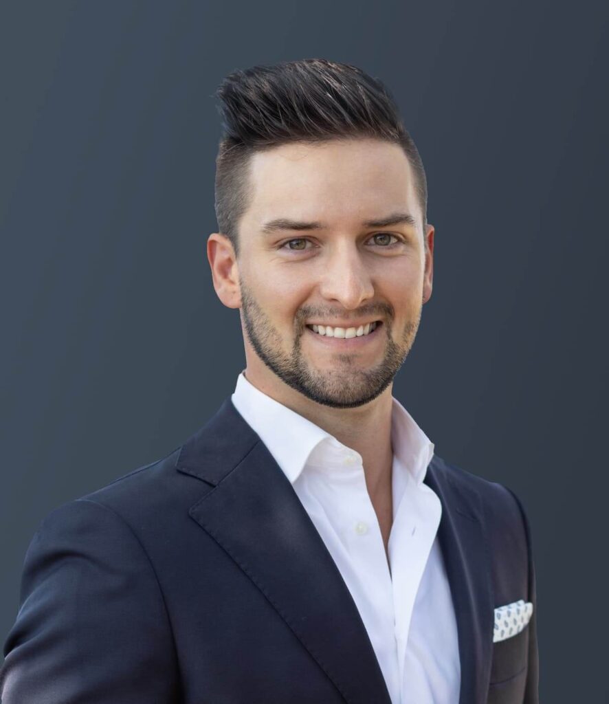 A man in a black suit and white shirt smiles against a gray background, exuding the confidence often found at Suncadia Resort.