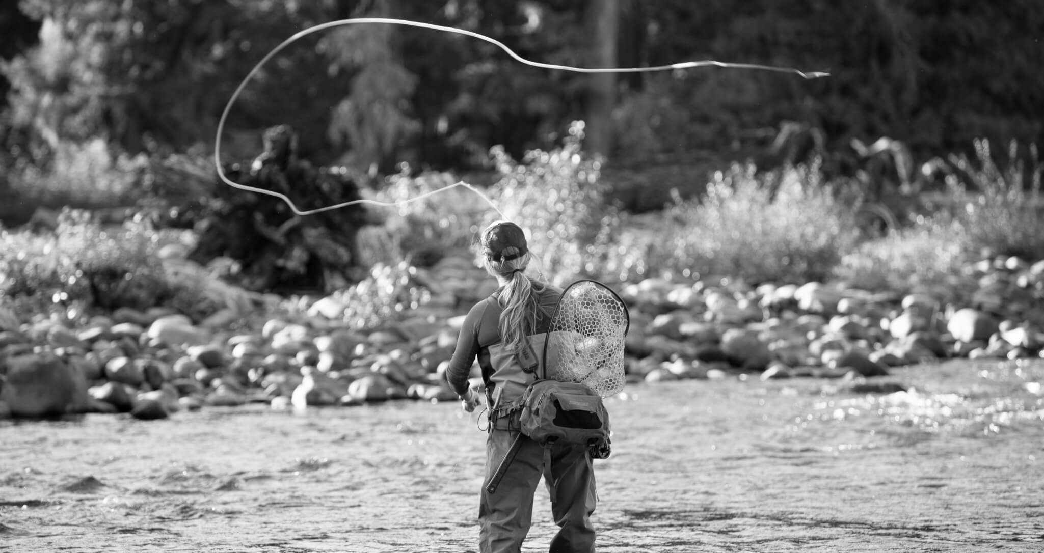 A person enjoys fly-fishing in a river, surrounded by rocks and trees near Suncadia Resort Washington, where nature offers tranquility amidst adventure.