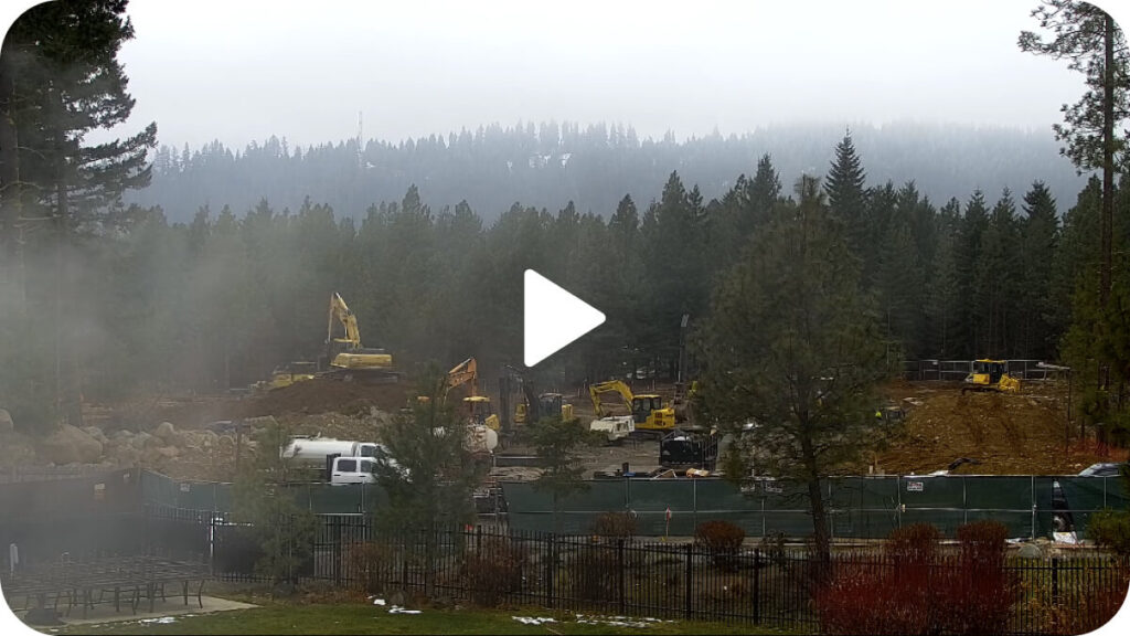 Construction site in a forested area with heavy machinery and vehicles, surrounded by trees and fog.