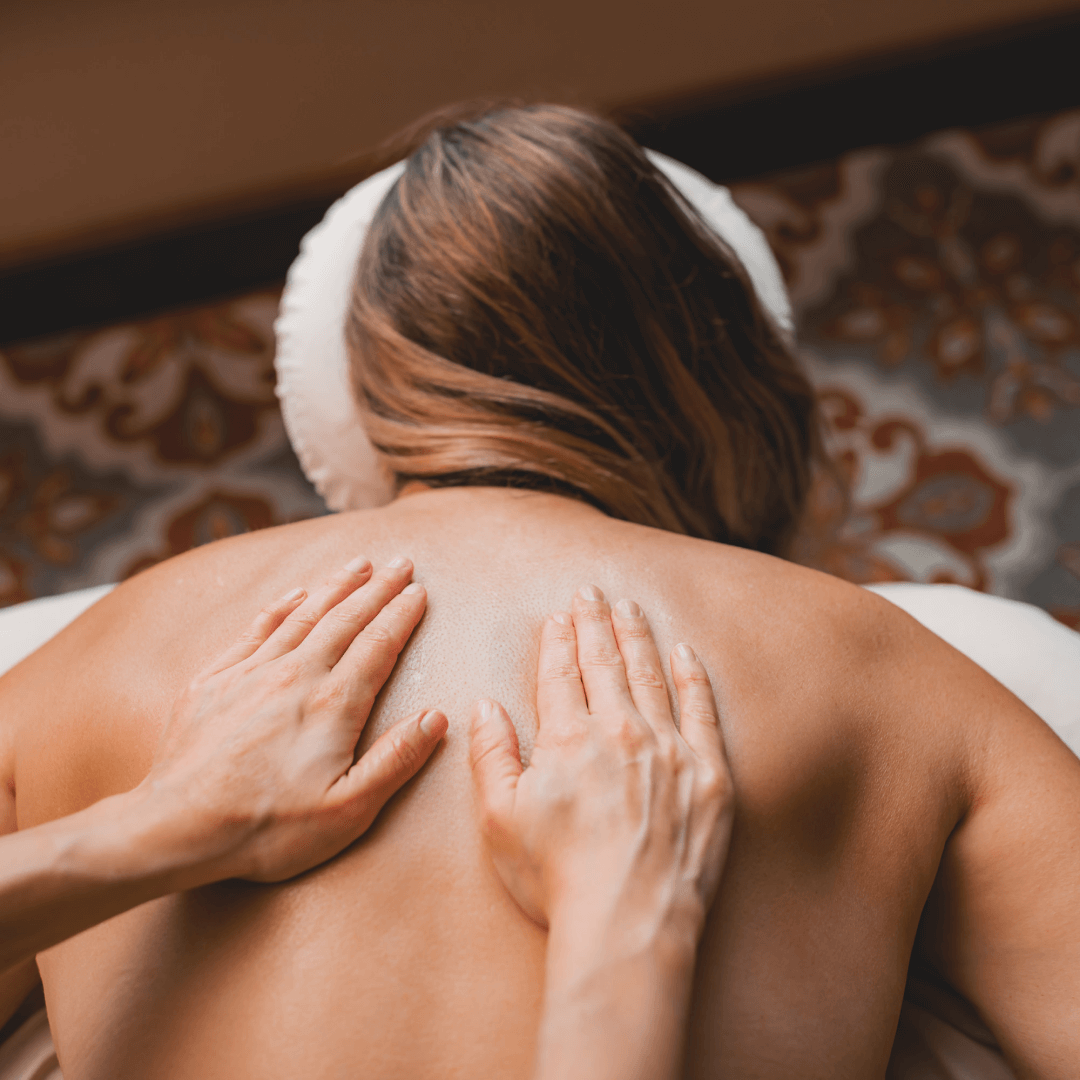 Person receiving a back massage while lying on a massage table, with hands applying pressure to their upper back.