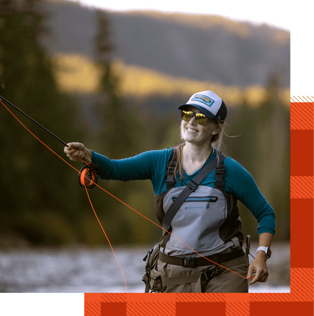 Person fly fishing in a river, wearing a cap, sunglasses, and waders, with a forested landscape in the background.