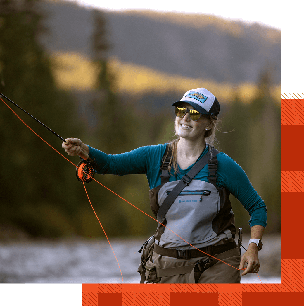 Person fly fishing in a river, wearing a cap, sunglasses, and waders, with a forested landscape in the background.