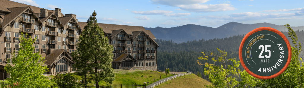 Lodge-style resort with wooden exterior on a hill, surrounded by trees and mountains, next to a 25th anniversary badge.