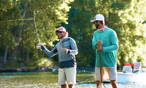 Two people stand in shallow water; one is casting a fishing line while the other holds a net. A boat and trees are visible in the background.