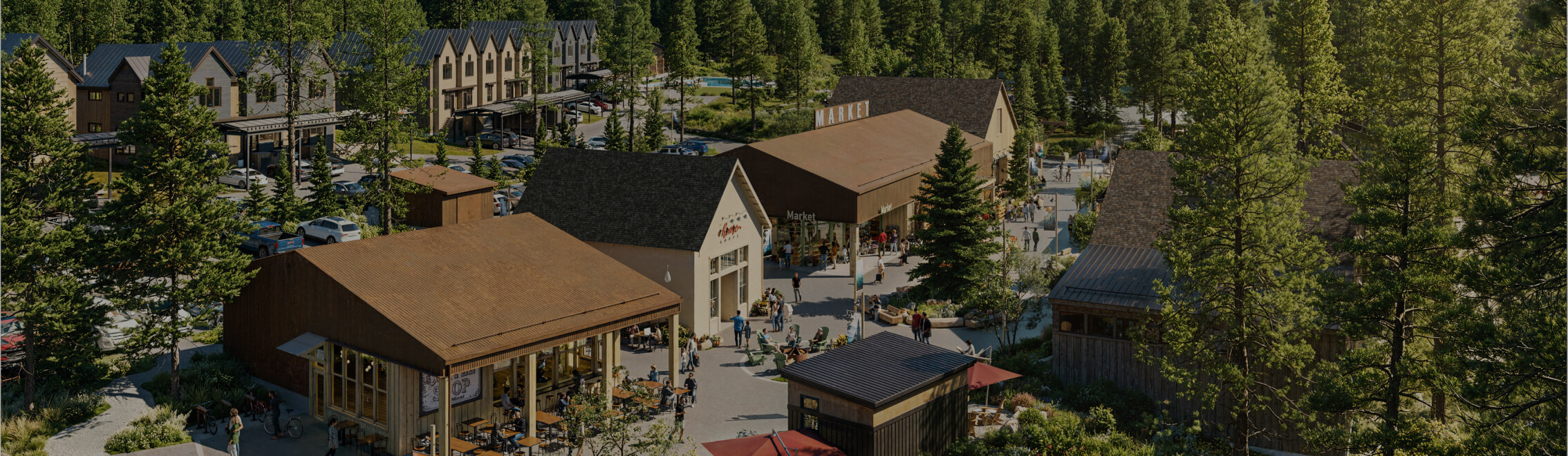 A small shopping and dining area with several wooden buildings surrounded by trees and parked cars, with people walking and sitting outdoors.