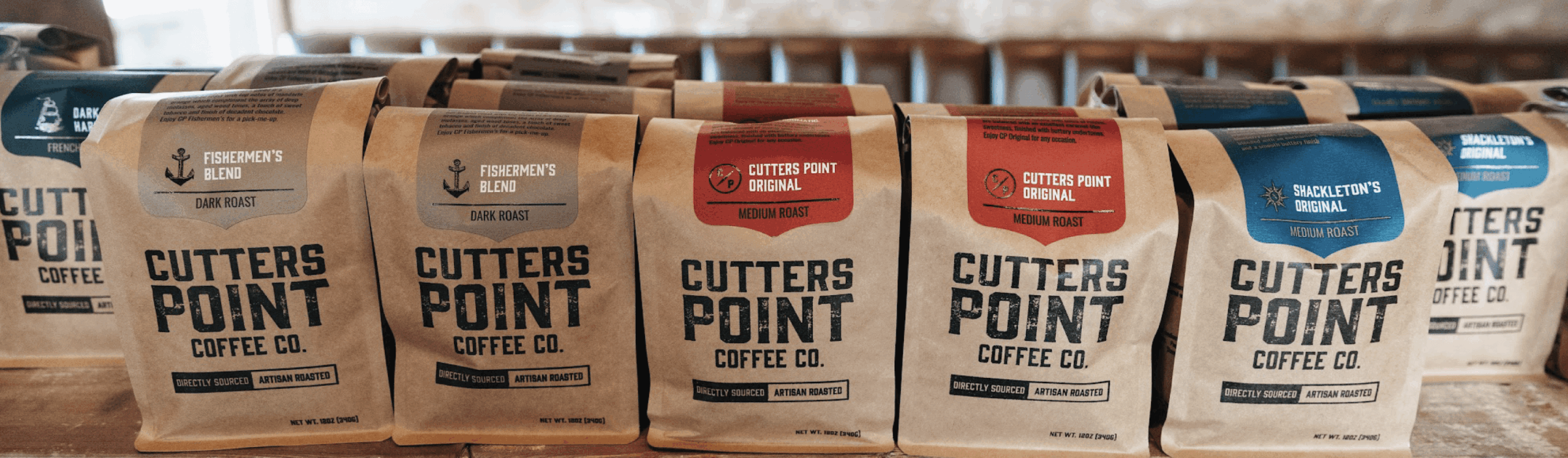 Bags of Cutters Point Coffee Co. in various blends, including Fishermen’s Blend, Cutters Point Original, and Shackleton’s Original, displayed side by side on a wooden surface.