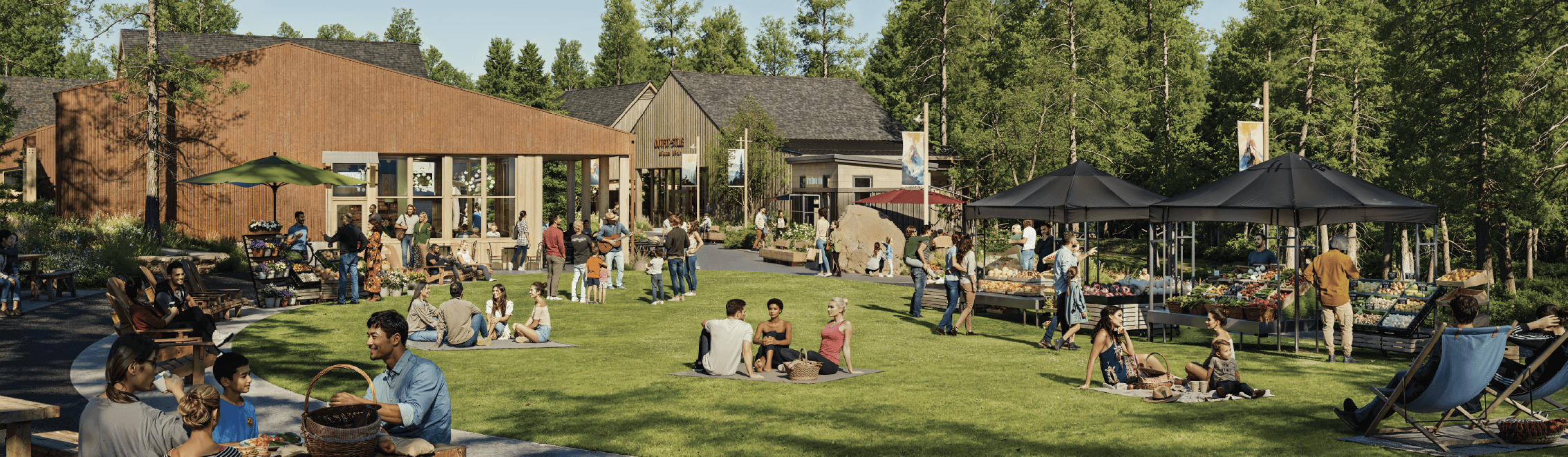 People gather at an outdoor community market with vendor stalls, picnic tables, and lawn seating on a sunny day, surrounded by trees and buildings.