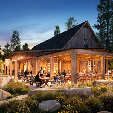 People dine at picnic tables outside a rustic wooden restaurant at dusk, surrounded by trees, rocks, and string lights.