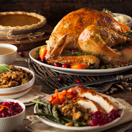 A table set with roast turkey, stuffing, cranberry sauce, green beans, sliced turkey, gravy, and a pumpkin pie in the background.