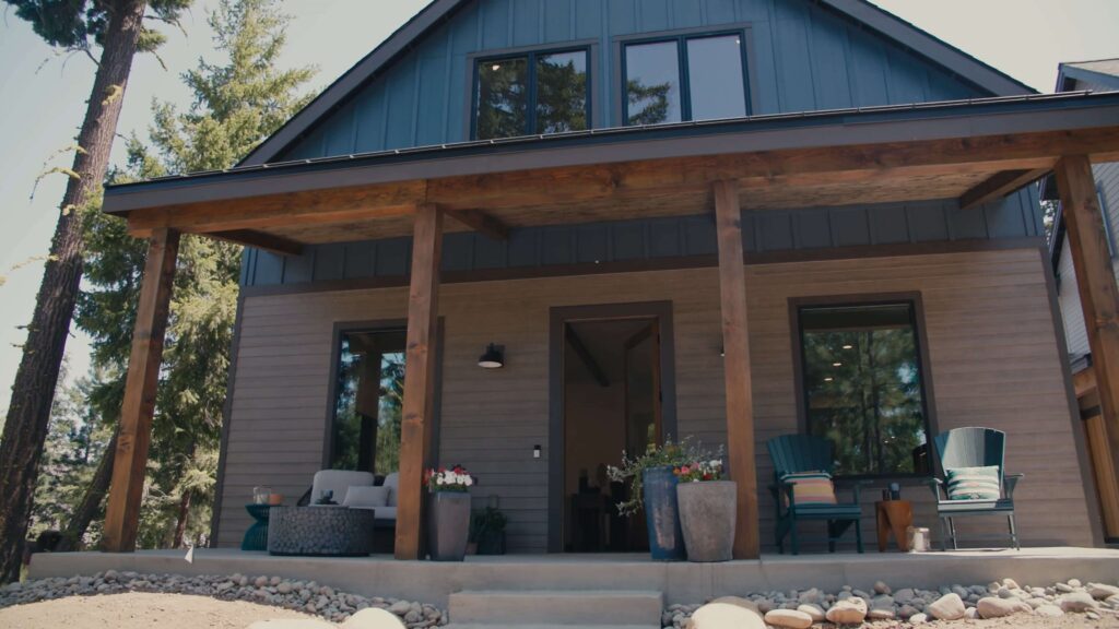 A modern two-story house in Suncadia Social with a covered porch, wooden pillars, large windows, outdoor seating, and potted plants on a stone-lined path.