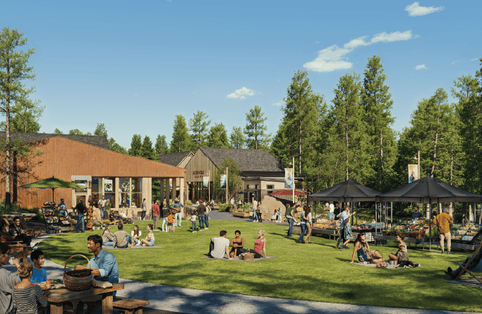 People gather and relax on a grassy lawn at a lively outdoor community event, surrounded by trees, food stands, and modern wooden buildings under a clear blue sky.