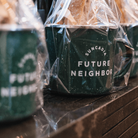 A close-up of green mugs wrapped in clear plastic, with the words Suncadia Future Neighbor printed on the front, displayed on a dark countertop.