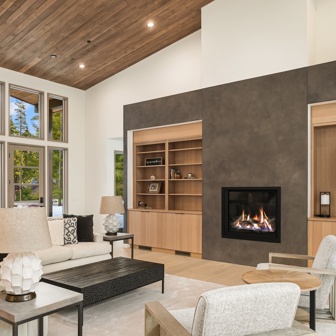 A modern living room with a beige sofa, wooden chairs, a black coffee table, built-in shelves, a fireplace set in a dark accent wall, large windows, and a wood-paneled ceiling.