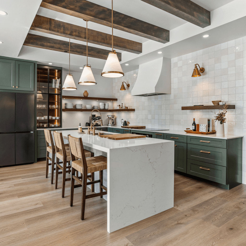 Modern kitchen with green cabinets, white marble island, wooden bar stools, pendant lights, open shelving with dishes, and wood ceiling beams. Light wood flooring and white tile backsplash complete the space.