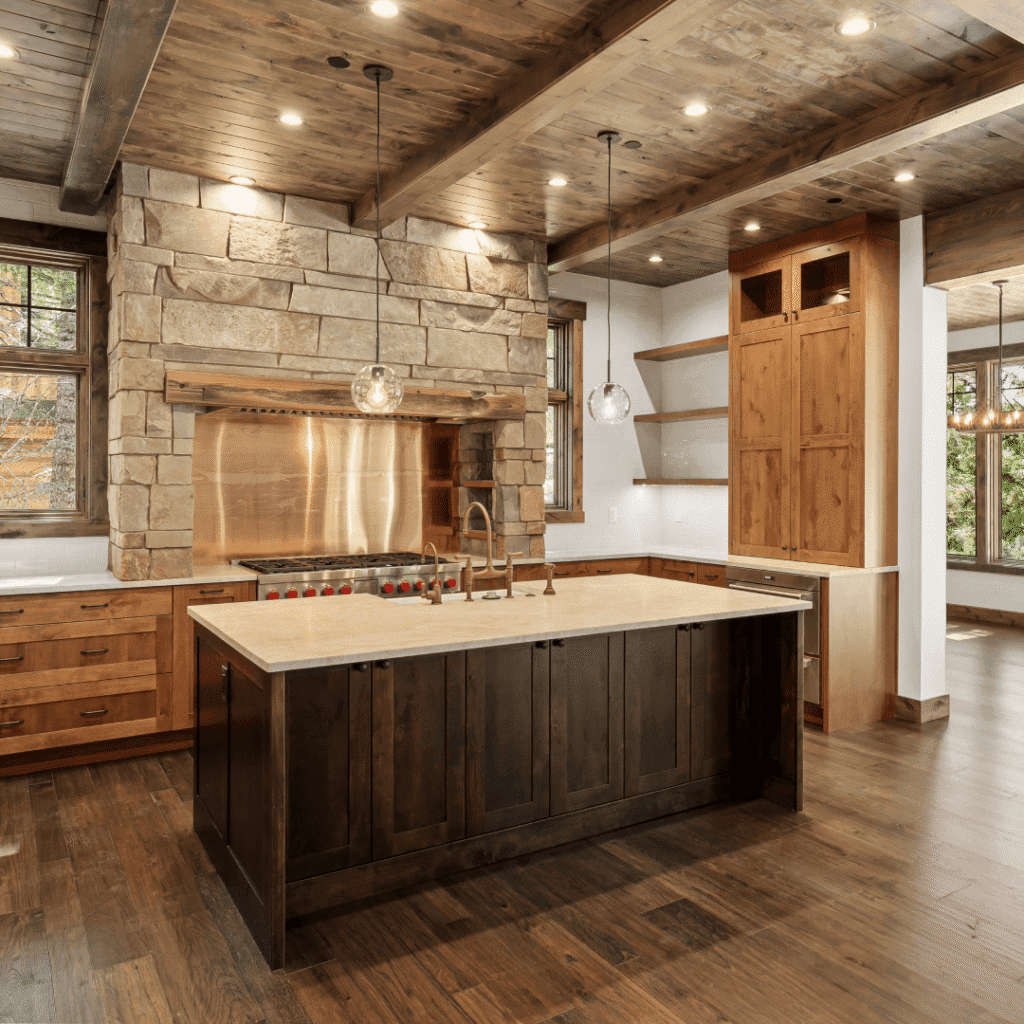 Rustic kitchen with wood floors, ceiling, and cabinets, a large stone range hood, modern stainless steel appliances, pendant lights, and an island with a built-in sink and dark wood base.