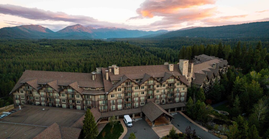 A large lodge-style hotel surrounded by dense forest and mountains at sunset, with a white van parked in front and soft clouds in the sky—an inviting retreat, especially during the Spring events at Suncadia.